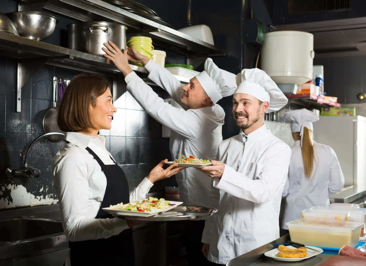 Chefs and server working in restaurant kitchen.